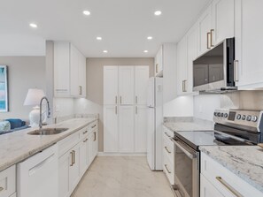 A modern kitchen with white cabinetry, a stainless steel sink, a built-in oven, and a microwave.