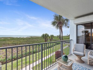 A balcony with a view of the ocean, a palm tree, and outdoor furniture.