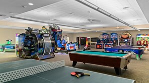 A recreation room with a pool table, ping pong table, and various arcade games including Halo and Jurassic Park.