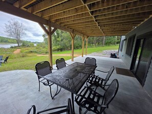 Eine überdachte Terrasse mit Tisch und Stühlen, die auf eine natürliche Landschaft mit Gewässer und Bäumen blickt.