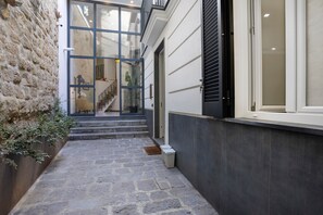 A narrow stone pathway leading to a staircase with a glass door entrance, a small trash bin, and a potted plant on the left. - Residenza Scale Napoletane - Deluxe Double Suite (Napoli)