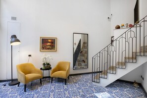 A room with a staircase, two armchairs, a floor lamp, a framed picture, and a small table with flowers. - Residenza Scale Napoletane - Deluxe Double Suite (Napoli)