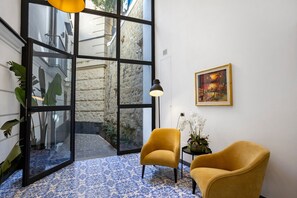 A room with a large glass door leading to an outdoor area, a yellow armchair, a small table with a lamp, and a framed painting on the wall. - Residenza Scale Napoletane - Deluxe Double Suite (Napoli)