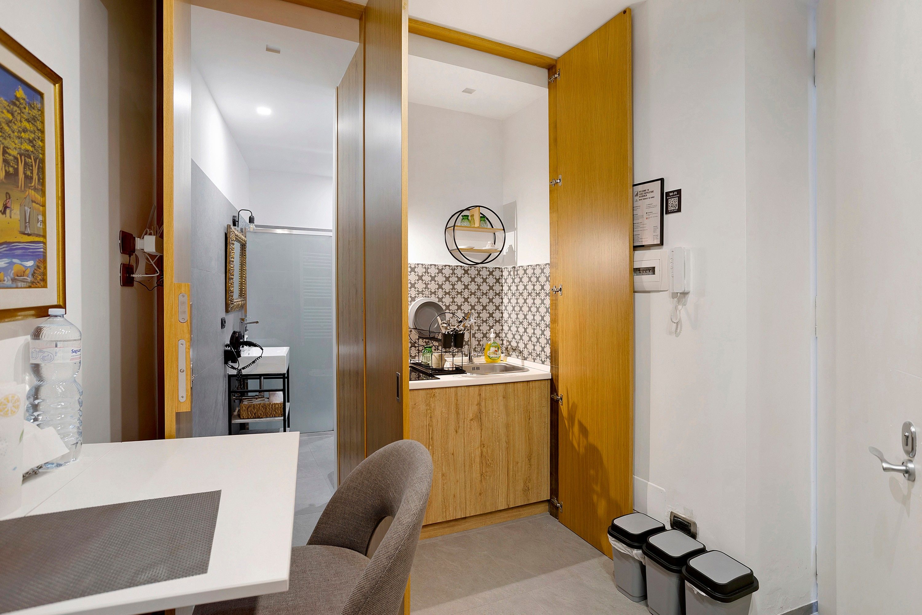 A compact hotel room with a dining area, a small kitchen, and a bathroom.