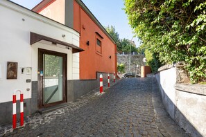 Eine Kopfsteinpflasterstraße mit einem Gebäude links und einem von Bäumen gesäumten Weg rechts.