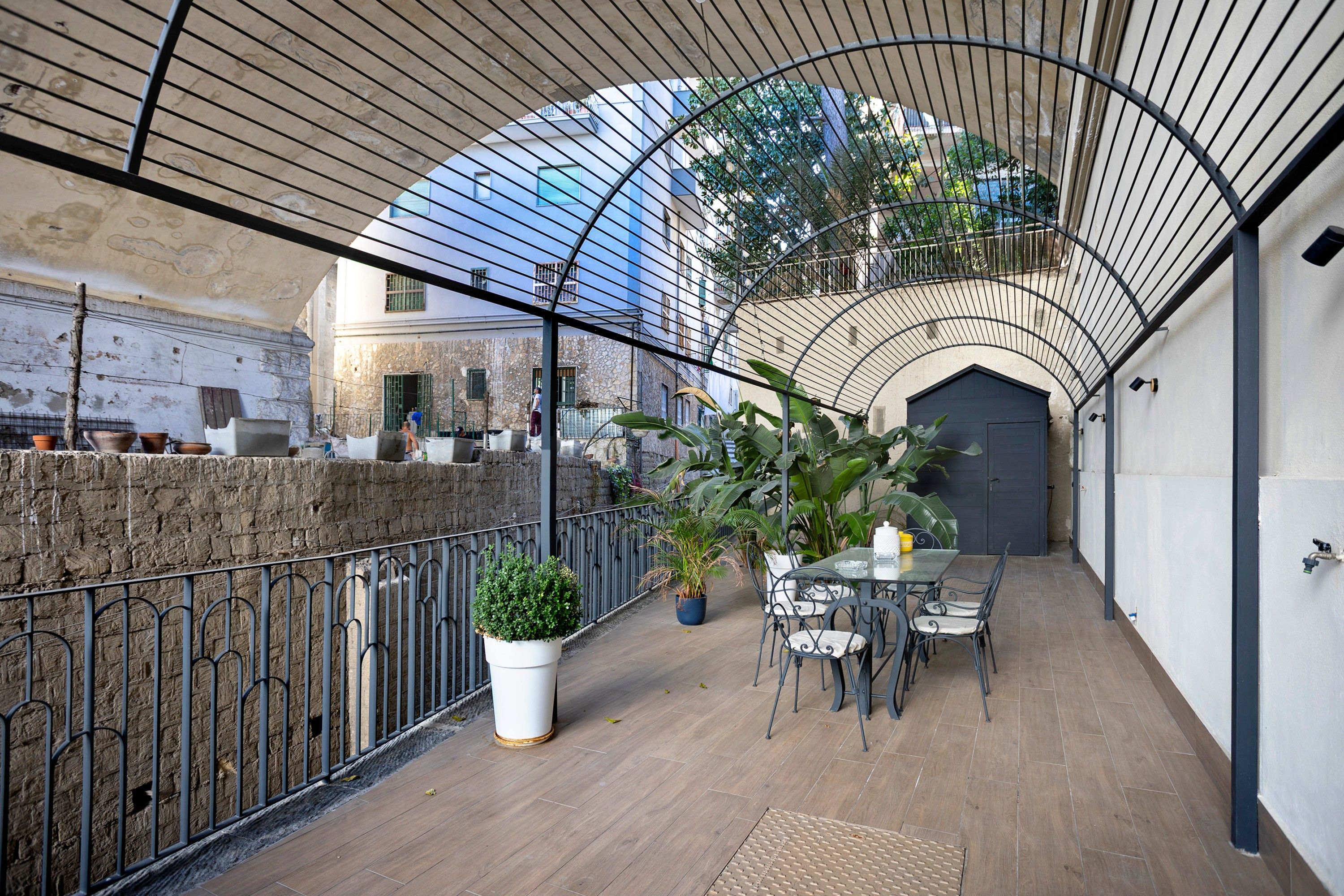An outdoor patio with a table and chairs, surrounded by a metal railing and potted plants.