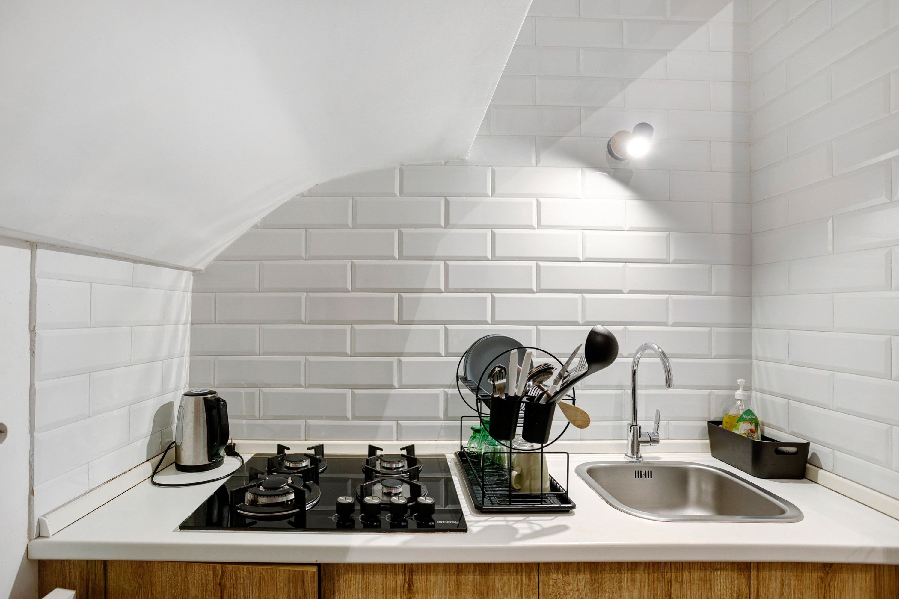 A kitchen with white tiled walls, a gas stove, a sink, and a coffee maker.