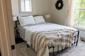 A bedroom with a bed, two bedside lamps, a window with a view, a door, and a wall-mounted wreath.