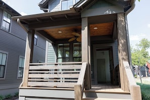 A wooden porch with a ceiling fan, a set of stairs leading to a door, and a view of the street.