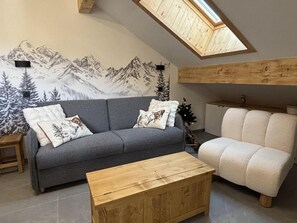 A cozy living room with a grey sofa, a wooden coffee table, and a white armchair. A mountain mural adorns the wall, and a skylight is visible above. - 350m from ski slopes, 3rd floor, balcony, parking, tv, ski locker, 36m², Valloire (Valloire)