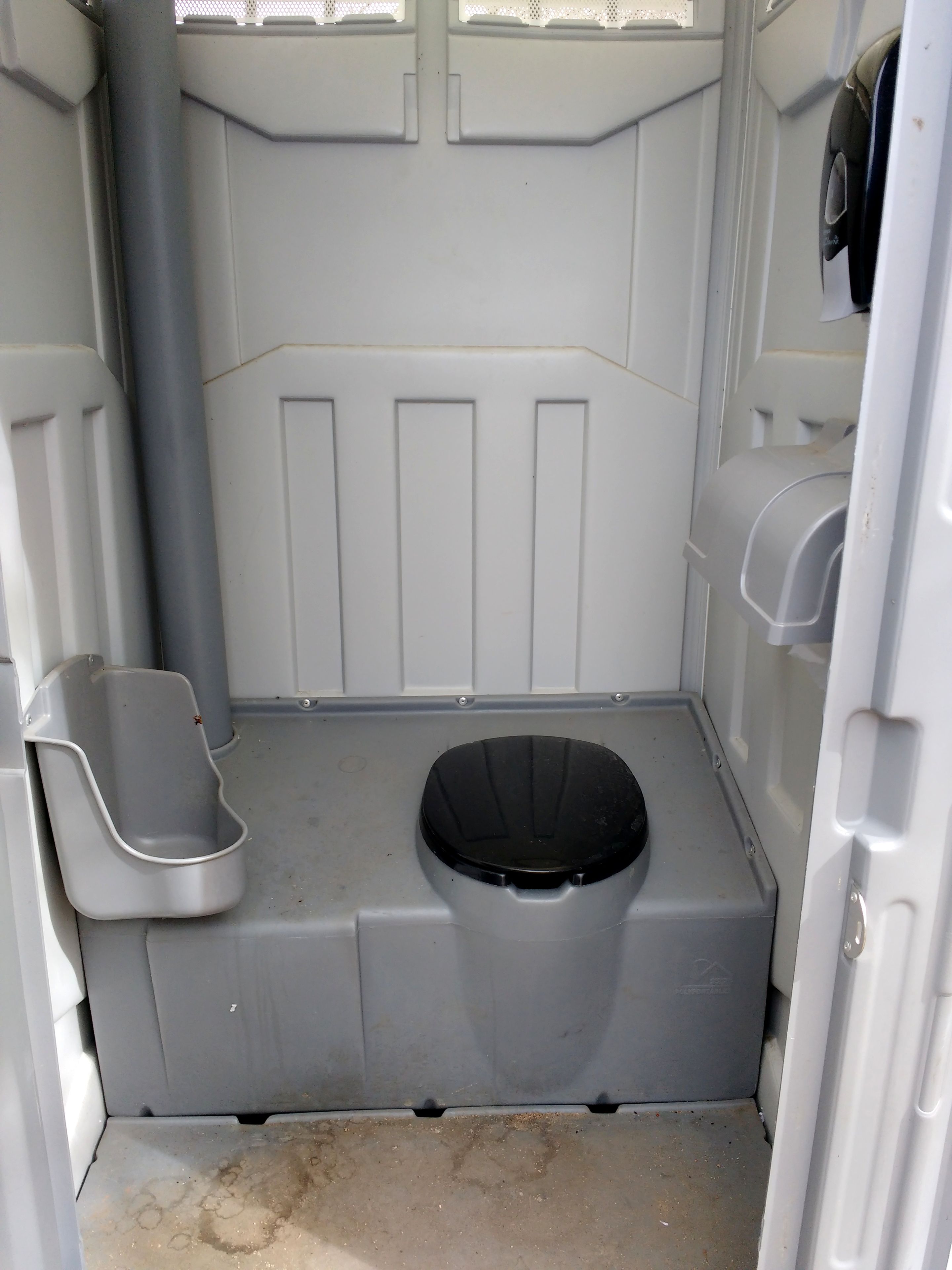 A compact, single-occupancy restroom with a grey floor, a black toilet seat, and a white urinal.