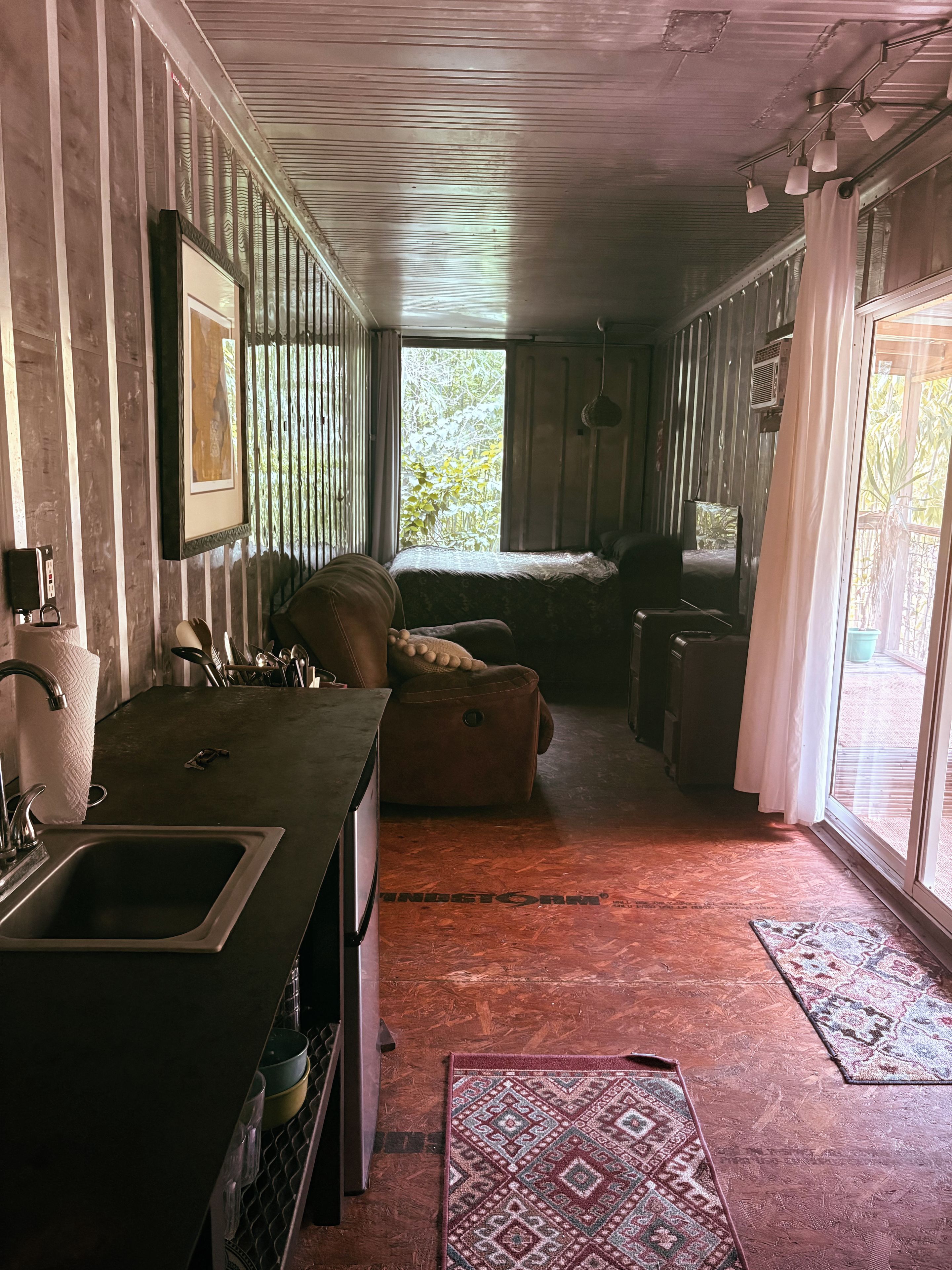 A cabin interior with a kitchen area, a sofa, and a window with curtains.