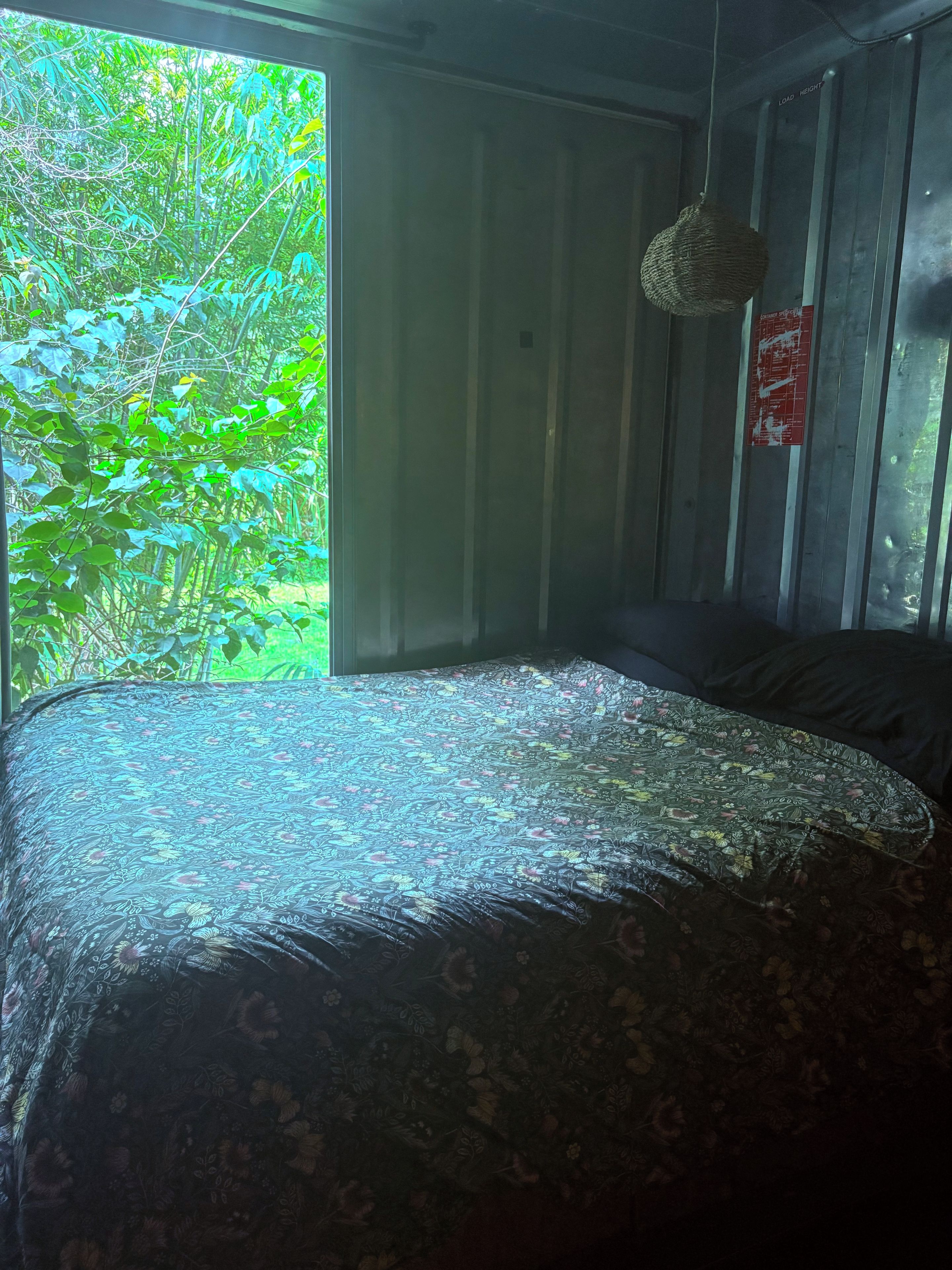 Une chambre avec un lit, une suspension décorative et une fenêtre donnant sur un paysage verdoyant.
