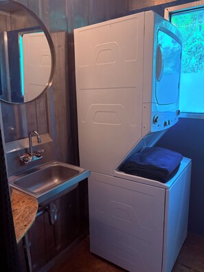 A compact laundry area with a sink, a mirror, and a washing machine.
