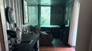 A narrow hallway leading to a living area with a sofa, a television, and a window with curtains. - Container home on bamboo farm with AC near Disney (Kissimmee)