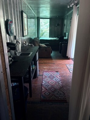 Un pasillo estrecho que conduce a una sala de estar con un sofá, un televisor y una ventana con cortinas.