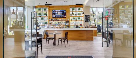 A bar area with a TV, shelves of bottles, and a counter. There are chairs and a table in the foreground.