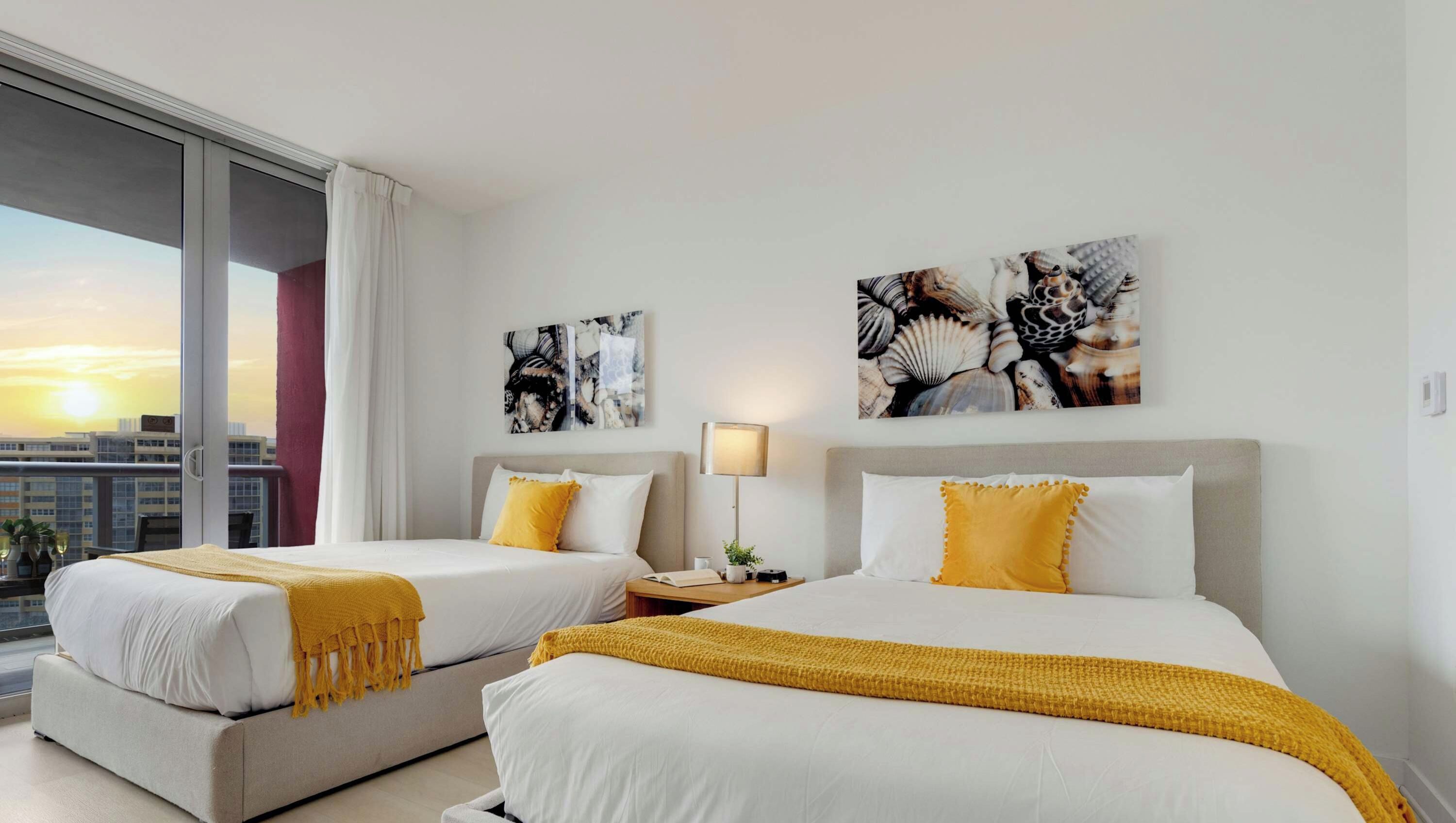 Habitación de hotel con dos camas, una mesita de noche, una lámpara y obras de arte en las paredes.