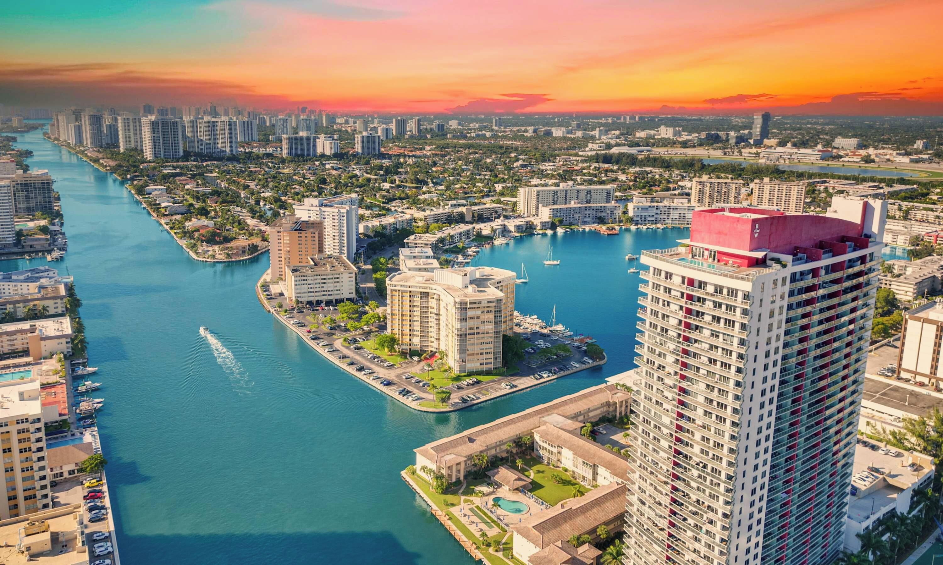 A high-rise building with a red roof, surrounded by a marina with boats, and a river running through the city.