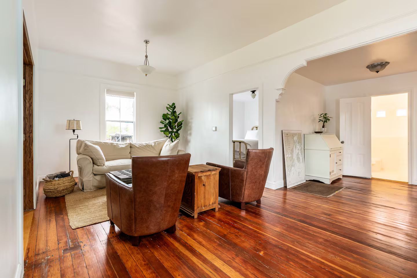 A spacious living room with a wooden floor, a sofa, two armchairs, a coffee table, and a lamp.