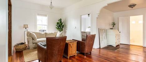 A spacious living room with a wooden floor, a sofa, two armchairs, a coffee table, and a lamp.