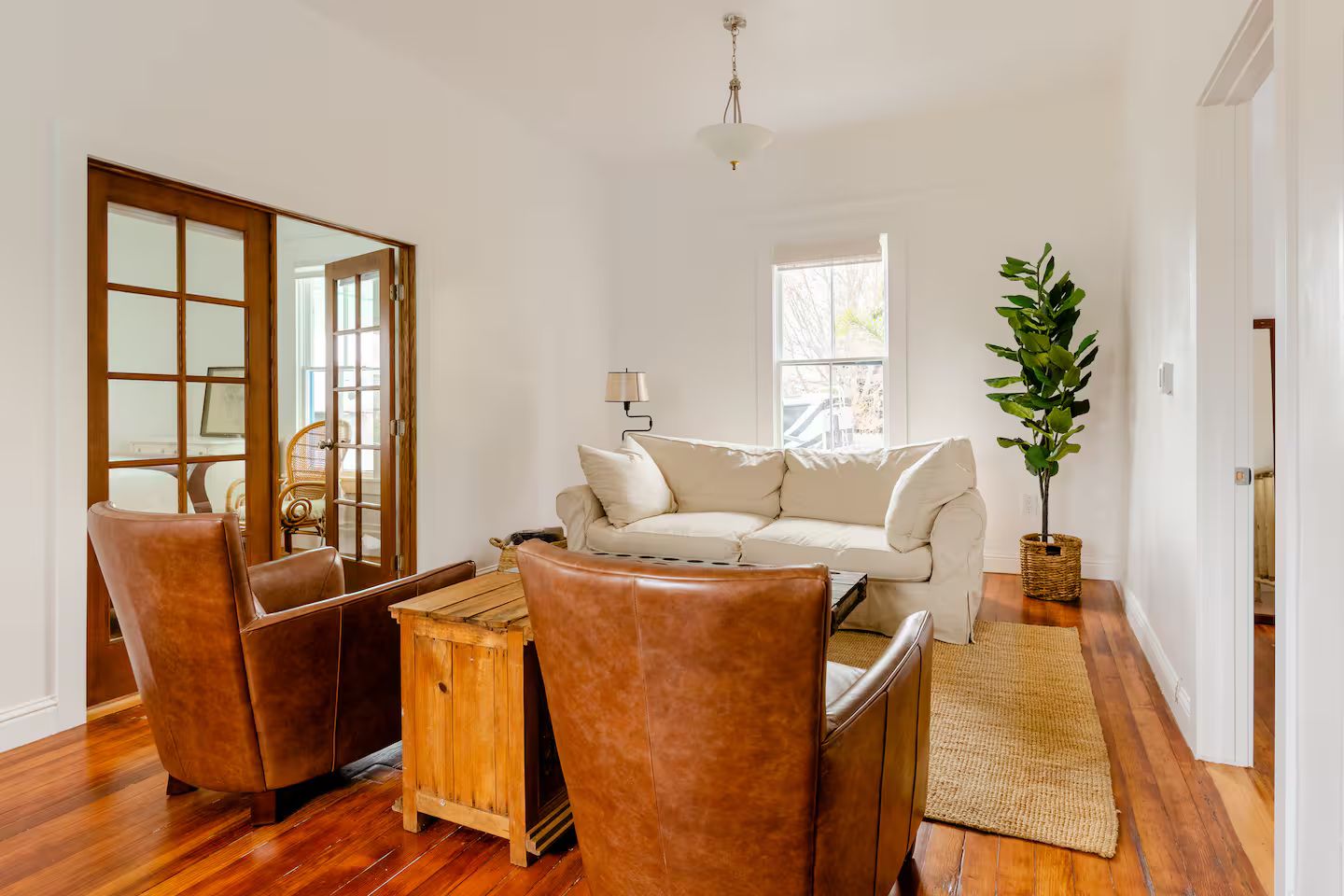 A room with a wooden floor, a white sofa, leather chairs, a wooden coffee table, a lamp, and a potted plant.