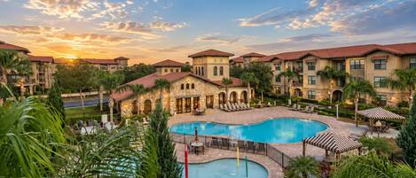A resort with a central swimming pool, multiple buildings with red-tiled roofs, and lush greenery.