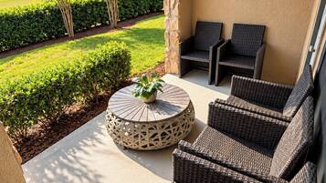 An outdoor patio with wicker furniture, a round table, and a view of a landscaped garden.