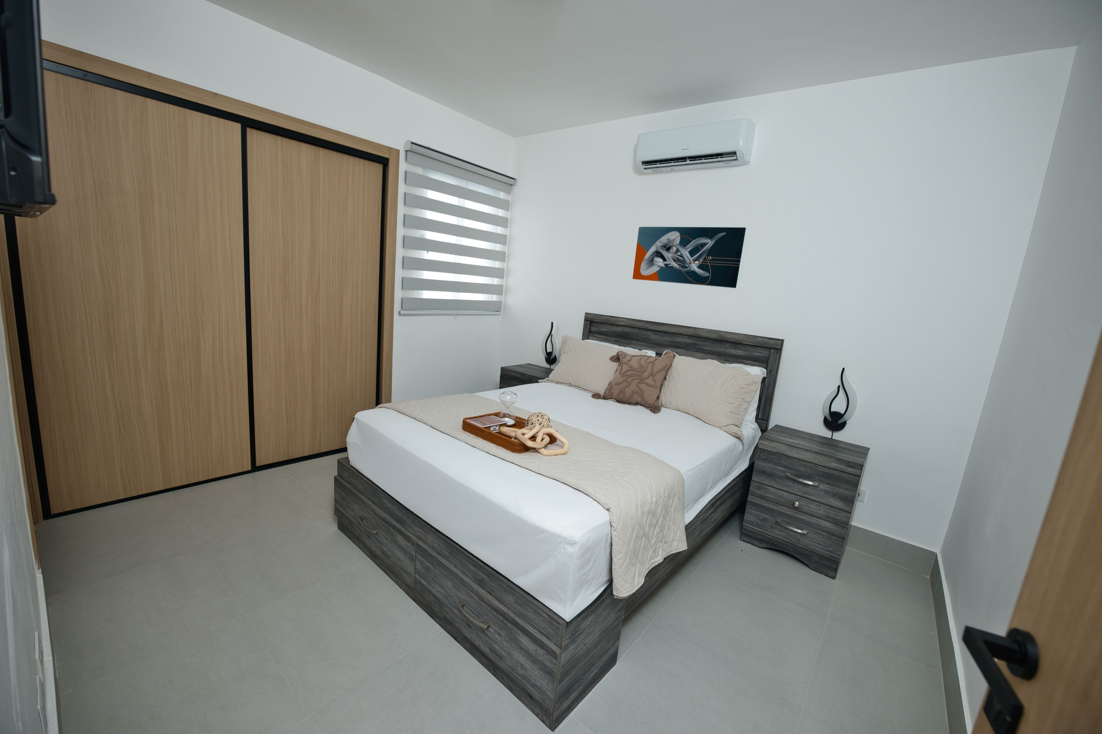 Ein Schlafzimmer mit einem Bett, Nachttischen, einem Kleiderschrank und einer Klimaanlage.