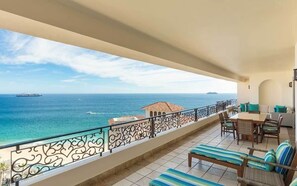 Un balcon avec vue sur la mer, un coin repas avec des chaises et une table, et un petit bâtiment avec un toit en tuiles.