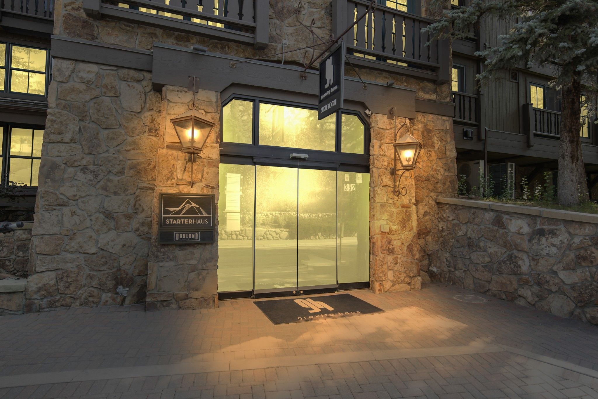 A hotel entrance with a stone facade, a glass door, and two wall-mounted lanterns.