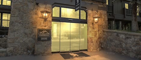 A hotel entrance with a stone facade, a glass door, and two wall-mounted lanterns.