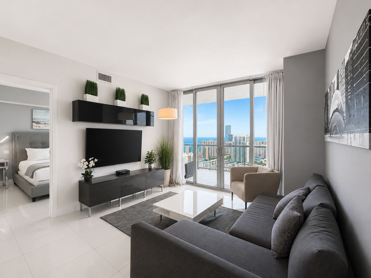 A modern living room with a flat-screen TV, a sofa, a coffee table, and a balcony with a city view.