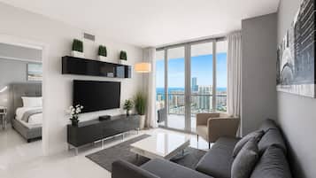 A modern living room with a flat-screen TV, a sofa, a coffee table, and a balcony with a city view.