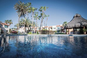 A swimming pool with palm trees and a thatched-roof structure, surrounded by hotel buildings. - Marina Penthouse ∙ Ocean View (La Paz)