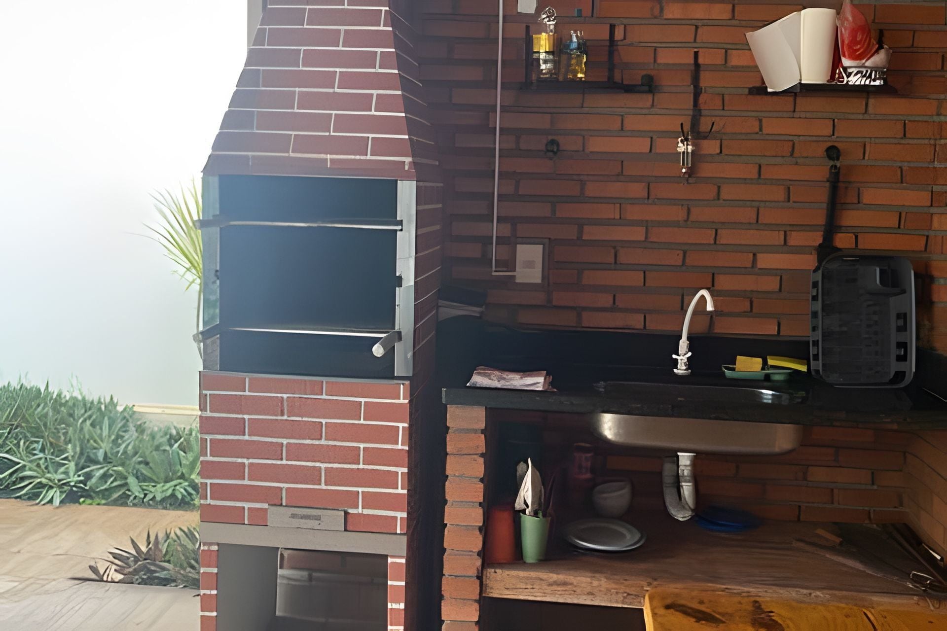 A brick oven with a window, a sink, and a shelf with bottles and a book.