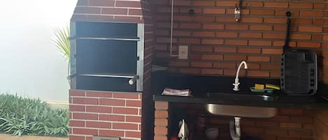 A brick oven with a window, a sink, and a shelf with bottles and a book.
