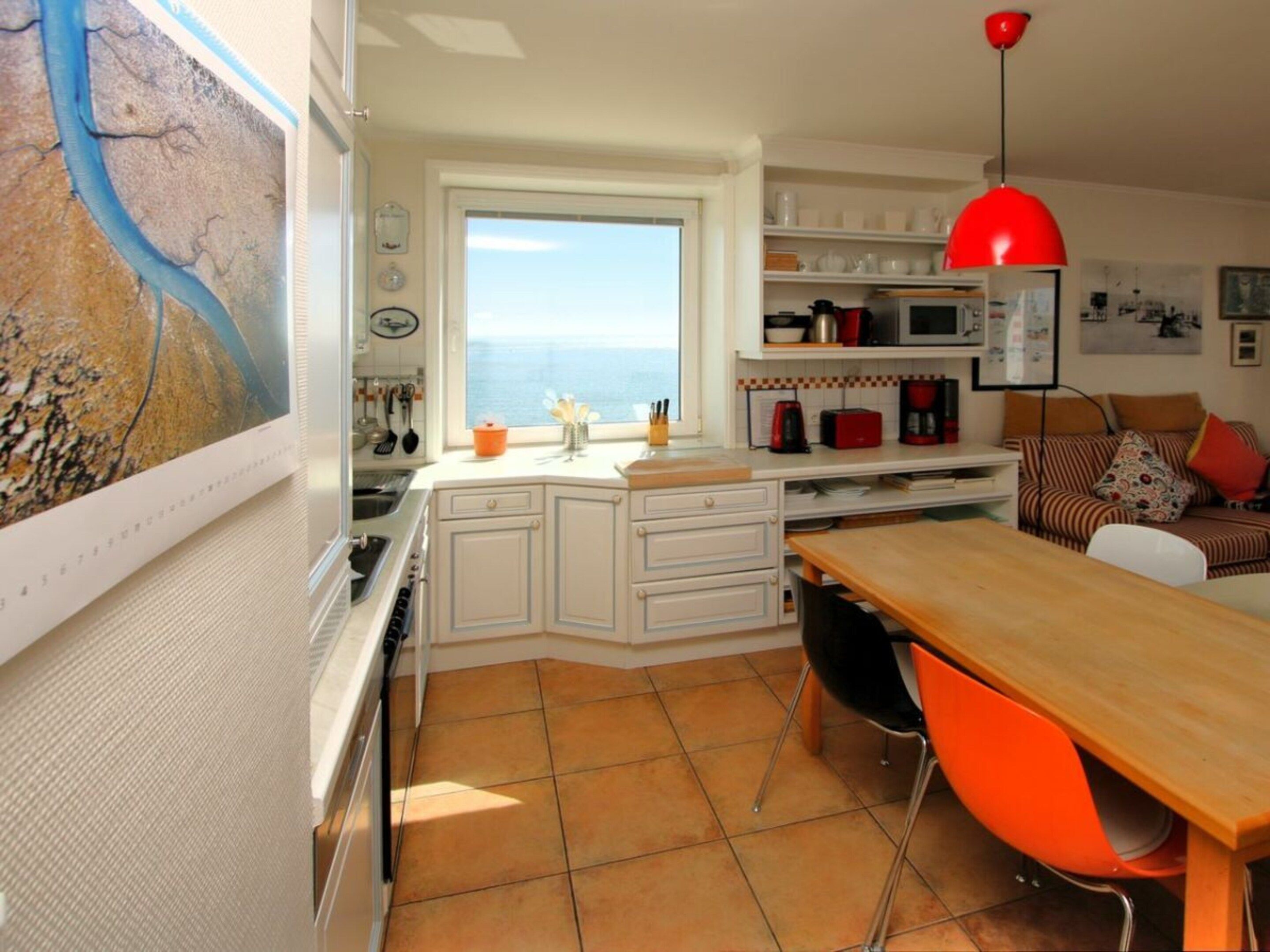 Cozinha compacta com área de refeições, vista para o mar e luminária pendente vermelha.