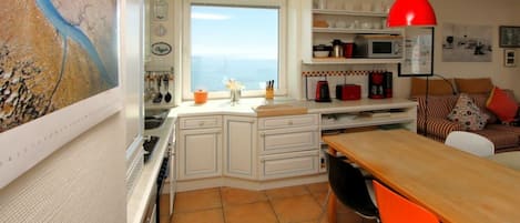 Cozinha compacta com área de refeições, vista para o mar e luminária pendente vermelha.