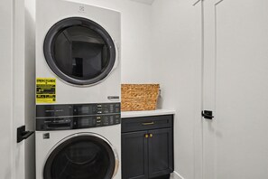 A laundry room with two front-loading washing machines, a dryer, and a small storage cabinet. - Golden Dome Retreat | 5BR | 0.7 Miles to ND (South Bend)