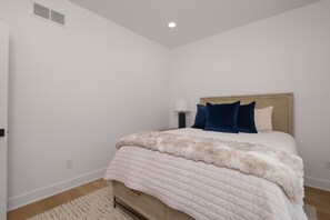 A bedroom with a bed, a nightstand, a lamp, and a window. - Golden Dome Retreat Upper Level Near Notre Dame (South Bend)