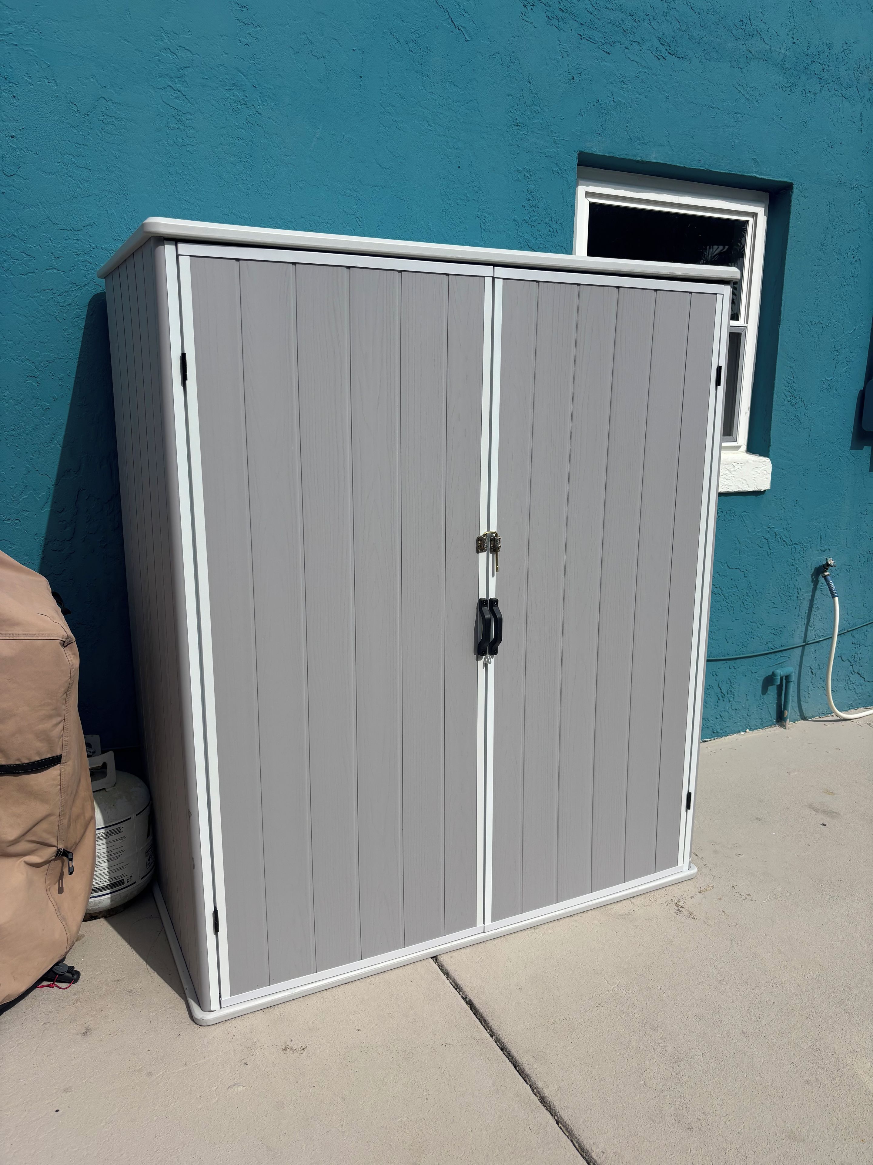 A grey storage cabinet with a white trim, a window, and a hose connected to the wall.