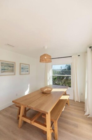 Una mesa de comedor de madera con bancos en una habitación con paredes blancas y un ventanal grande.