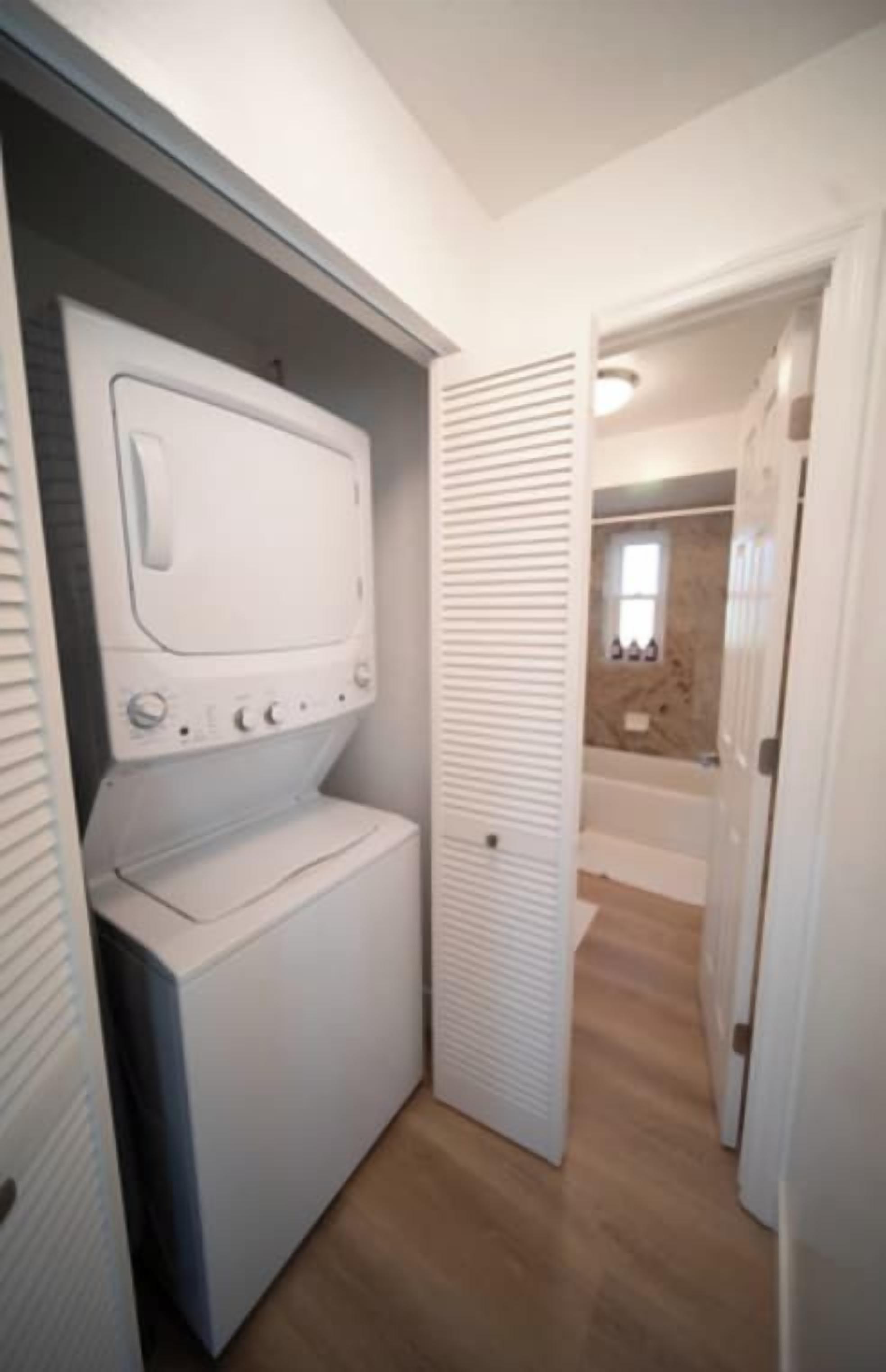 A laundry room with a washing machine and dryer, a door leading to a bathroom, and a wooden floor.
