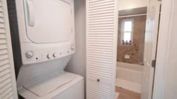 A laundry room with a washing machine and dryer, a door leading to a bathroom, and a wooden floor.