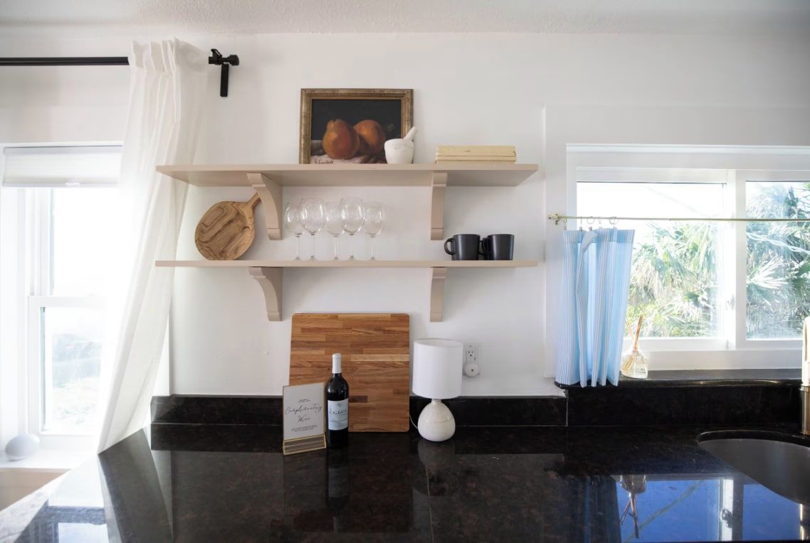 Una cocina con encimera negra, repisas de madera, una botella de vino y un marco de fotos.