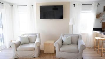 Una sala de estar con dos sillones, una pequeña mesa auxiliar de madera y un televisor de pantalla plana montado en la pared.