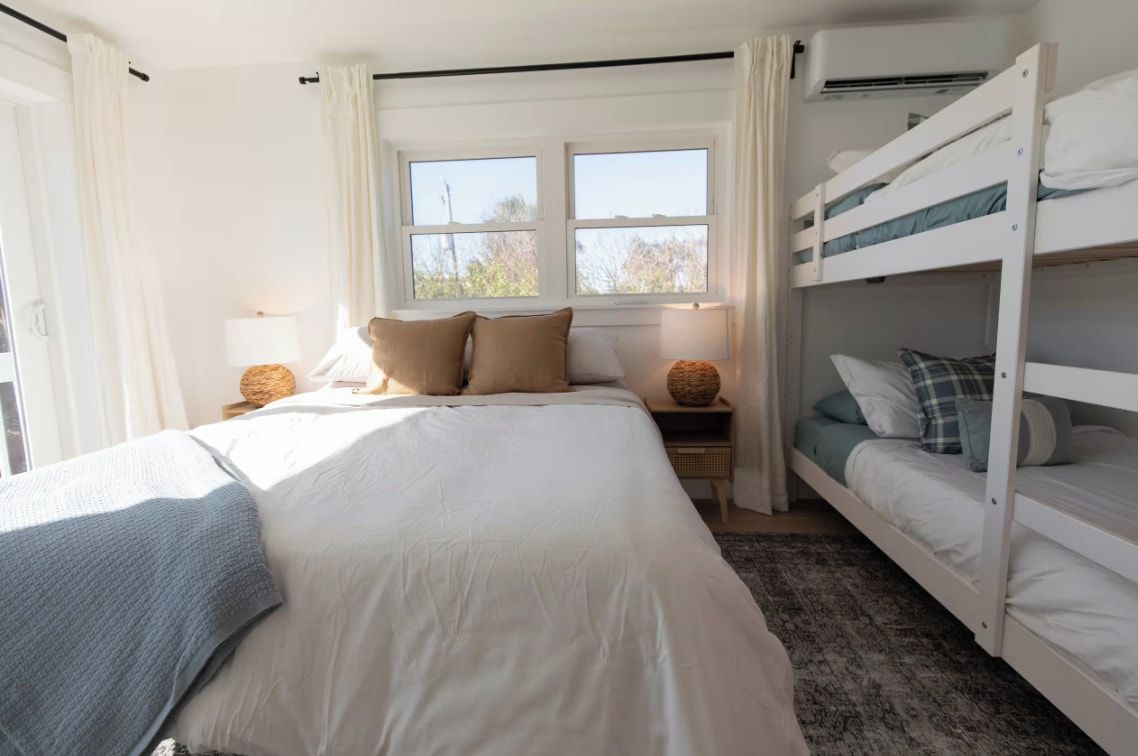 Un dormitorio con una cama individual, una litera, una ventana con cortinas, una lámpara de noche y un aire acondicionado instalado en la pared.