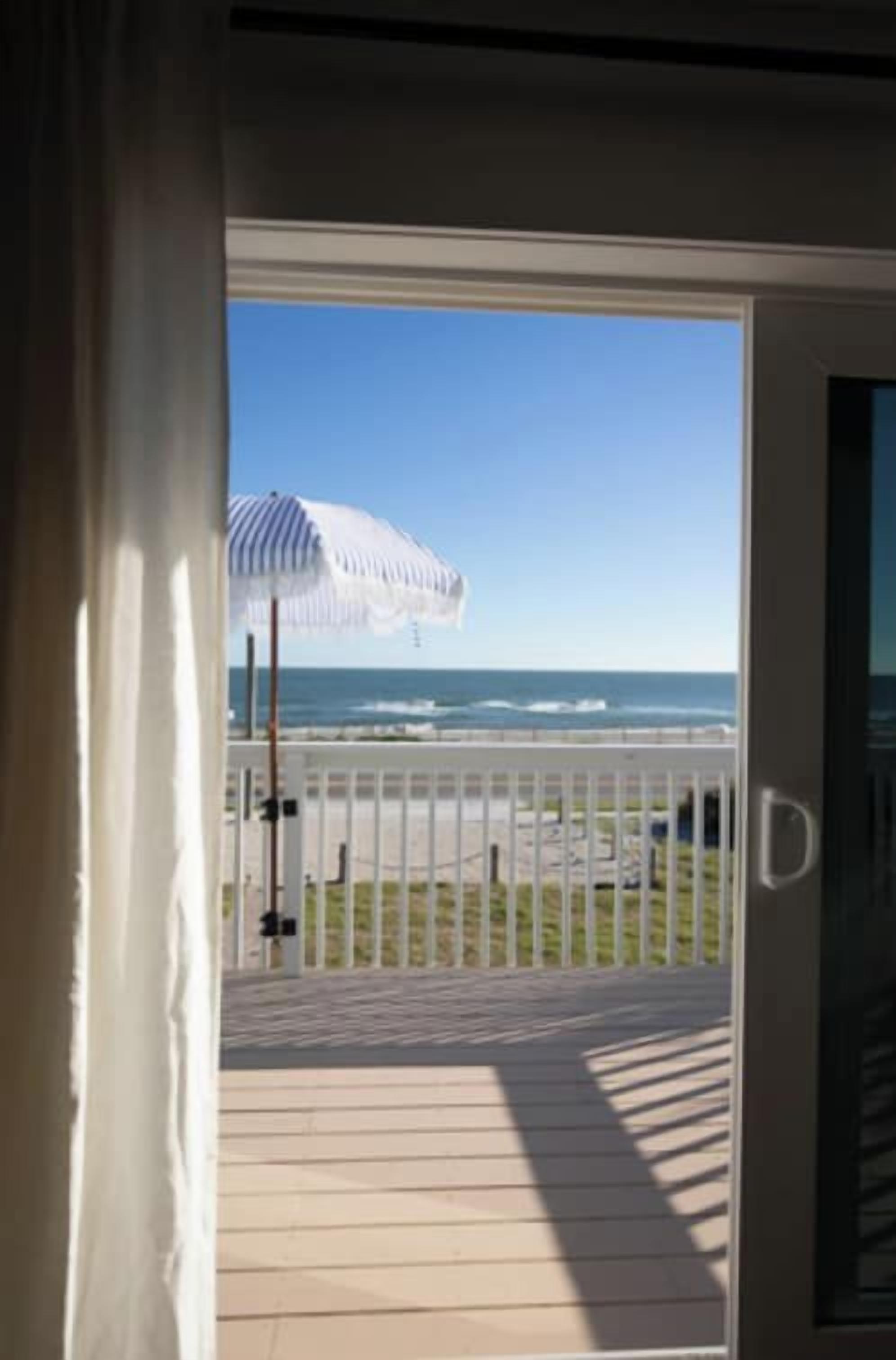 A view from a room to a balcony with a white umbrella, a railing, and a clear sky.