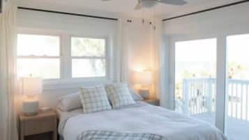 A bedroom with a bed, bedside lamps, a ceiling fan, and a view of the outdoors.